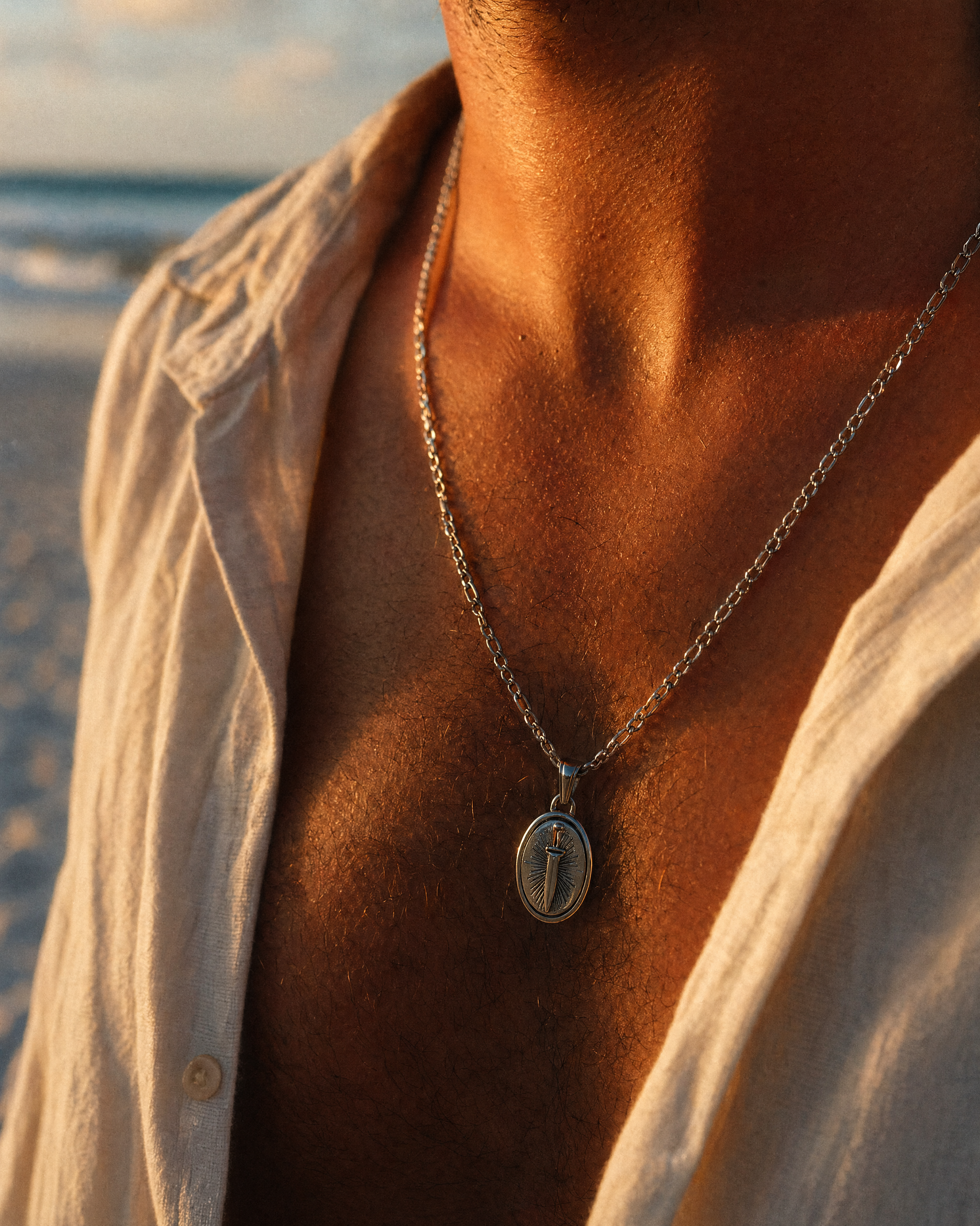 Silver stainless steel dagger pendant necklace worn on a man's chest, close-up of oval pendant