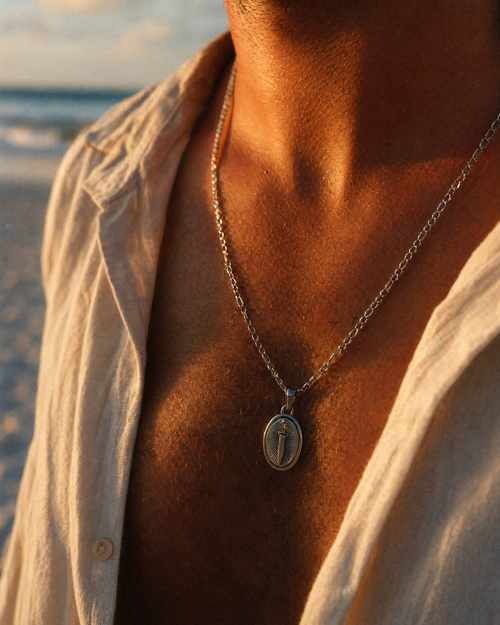 Silver stainless steel dagger pendant necklace worn on a man's chest, close-up of oval pendant